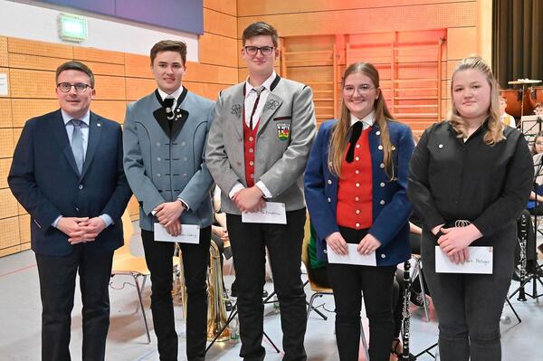 Bild vergr&ouml;&szlig;ern: Das Foto zeigt Landrat Christoph Schauder bei der Ehrung von vier junge Musikerinnen und Musiker: Valerie Metzger (v.r.n.l.), Merle Köhl, Kai Kimmelmann und Valentin Gehrig. Sie haben bereits zum fünften Mal beim Kreisjugendblasorchester teilgenommen und erhielten dafür eine Ehrennadel sowie einen Gutschein des Musikhauses Martens in Schrozberg.