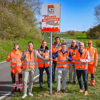 Die Beschilderung an den Landkreisgrenzen des Main-Tauber-Kreises wird schrittweise ausgetauscht. Ahorns B�rgermeister Benjamin Czernin, Landrat Christoph Schauder und Technik-Dezernent Werner R�ger (vordere Reihe von links) gaben den Startschuss an der Kreisstra�e K 2885 und freuen sich gemeinsam mit den Mitarbeitern des Stra�enbauamts �ber das neue Design der Schilder.