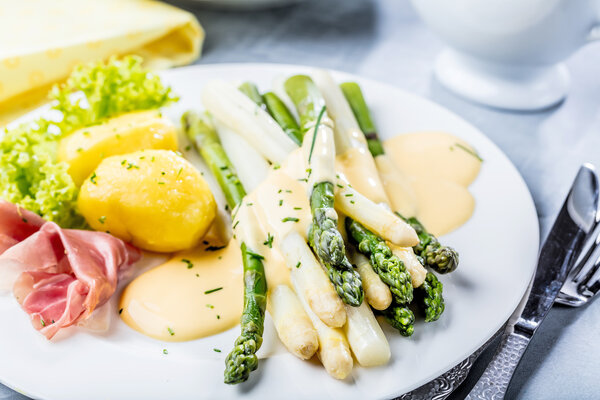 Das Bild zeigt einen Teller mit Kartoffeln, Schinken, wei&szlig;em und gr&uuml;nem Spargel. 