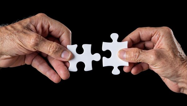 Das Foto zeigt zwei H&auml;nde, die zwei passende Puzzle-Teile zusammen halten.