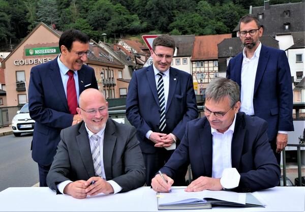 �ber die Unterzeichnung des Verwaltungsabkommens zum Neubau der Mainbr�cke freuen sich (stehend von links) MdL Prof. Dr. Wolfgang Reinhart (Baden-W�rttemberg), die Landr�te Christoph Schauder (Main-Tauber-Kreis) und Jens Marco Scherf (Landkreis Miltenberg), der MdL Berthold R�th (Bayern) sowie (sitzend) die beiden Unterzeichner B�rgermeister Roger Henning (Stadt Freudenberg) und B�rgermeister Andreas Freiburg (Gemeinde Collenberg).