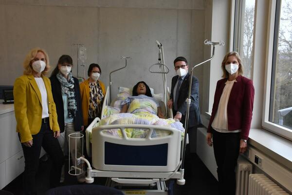 Bild vergr&ouml;&szlig;ern: Das Foto zeigt Dezernentin Ursula Mühleck, Stellvertretende Schulleiterin Marlies Bauer, Fachlehrerin Sandra Schler, Landrat Christoph Schauder und Schulleiterin Anke Mund am Bett von Nursing Anne: Die Pflegepuppe wird an der EPE für die generalistische Pflegeausbildung eingesetzt.