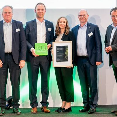 Nahmen stellvertretend f�r die Belegschaft einen der hei�begehrten IKU 2022 entgegen (v.l.n.r.): Uwe Rothaug (Gesch�ftsf�hrer), Matthias Hofmann (Gesch�ftsf�hrer), Lisa Knoops (Projektleiterin) und Ralph Knecht (CEO). Rechts au�en: Oliver Krischer, Parlam