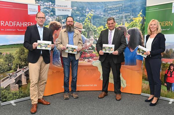 Peter Hellerbrand und Christian Bach von den Fr�nkischen Nachrichten �bergeben die druckfrische Brosch�re "Liebliches Taubertal erleben" an Sven Dell und Ursula M�hleck (von links) vom Tourismusverband "Liebliches Taubertal": Auch 2022 gibt es die Tourismus- und Kulturzeitung.