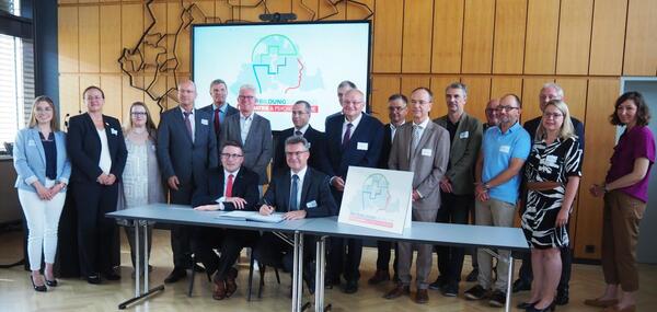 Bei der Unterzeichnung der Kooperationsvereinbarung f�r den Weiterbildungsverbund Psychiatrie: die beiden Landr�te Christoph Schauder (Main-Tauber) und Dr. Achim Br�tel (Neckar-Odenwald, sitzend von links) im Kreise der Vertragspartner und Projektbeteiligten.