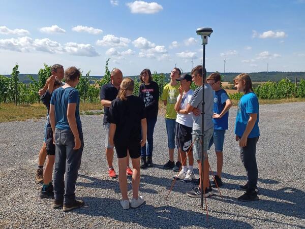 Bild vergr&ouml;&szlig;ern: Das Foto zeigt Dirk Nied, der den Schülerinnen und Schülern aus Külsheim die Handhabung des Satellitenmessgerätes erklärt: Bei der "Aktionswoche Geodäsie" haben die Teilnehmenden interessante Einblicke in den Beruf die Vermessungstechnik erhalten.