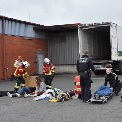 Bild vergr&ouml;&szlig;ern: Das Bild zeigt Verletzte, die in einer Reihe auf dem Boden liegen und Einsatzkräfte, die sie versorgen.