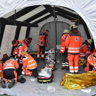 Bild vergr&ouml;&szlig;ern: Das Bild zeigt ein Zelt für Verletzte, welches gerade von Hilfskräften des Roten Kreuzes eingerichtet wird.
